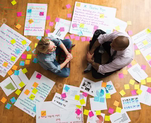 Preview: Colleagues Sitting Cross Legged On Floor With Papers And Adhesive Notes