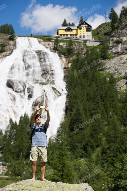 Preview: Young Man Taking Smartphone Selfie In Front Of Toce Waterfall, Formazza, Verbania, Piemonte, Italy