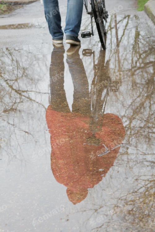 Preview: Reflection Of Man With Bicycle In Puddle