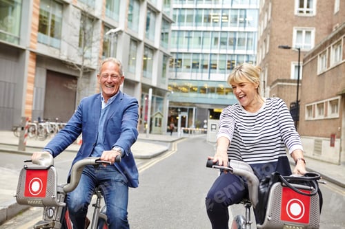 Preview: Mature Dating Couple Laughing Whilst Cycling On Hire Bicycles, London, Uk
