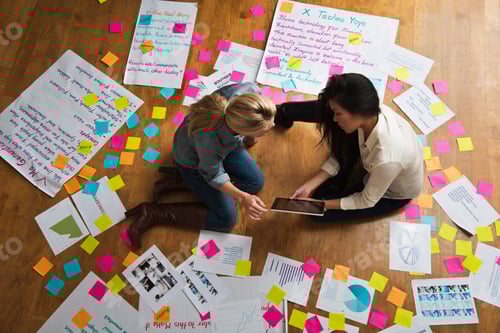 Preview: Colleagues Sitting On Floor With Digital Tablet, Papers And Adhesive Notes