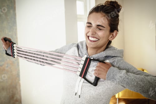 Preview: Young Woman Straining To Exercise With Chest Expander In Living Room