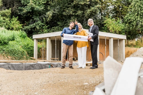 Preview: Couple On Construction Site Discussing Blueprints With Architect, Looking Up Pointing