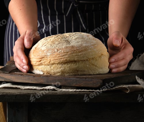 Preview: Female Hands Holding Round Baked Wheat Flour Bread Over Wooden Table, Close Up