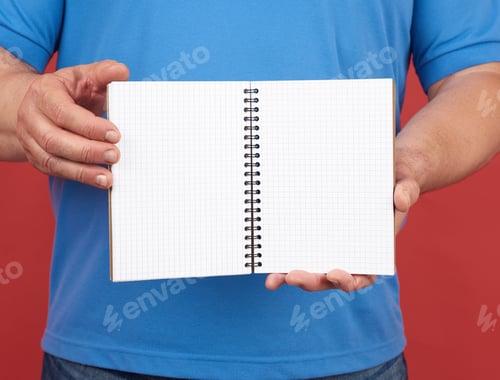 Preview: Man In Blue Clothes Holds An Open Spiral Notebook With Blank White Sheets, Red Background