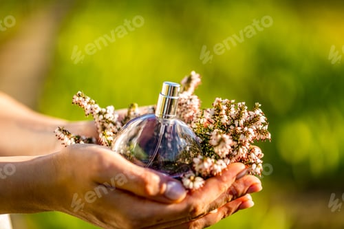 Visualização: Mulher jovem e bonita com frasco de perfume floral. Vista aproximada das mãos de uma mulher mostrando perfume.