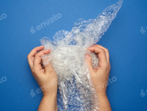 Preview: Female Hand Holding Crumpled Piece Of Polyethylene With Air Bubbles On A Blue Background, Packing