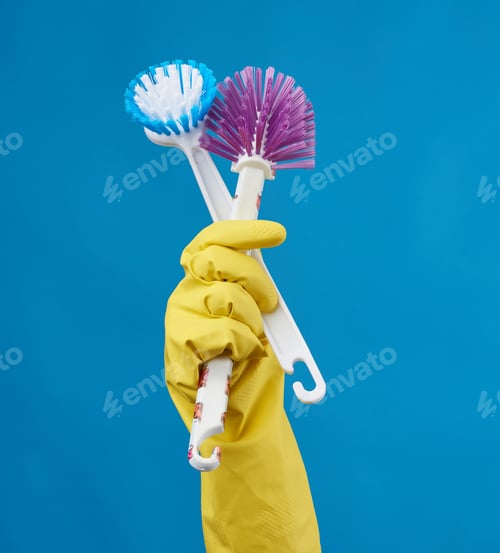 Preview: Hand In A Yellow Rubber Glove For Cleaning A House Holds Two Plastic Brushes With A Handle On A