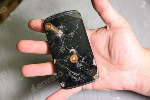 Preview: Man Holding Crashed Black Smartphone With A Bullet In Hand. Broken Lcd Touch Screen. Information