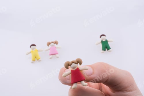 Preview: Hand Holding Colorful Dressed Children Figure On A White Background