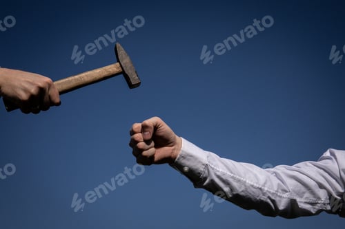 Preview: Hand Holding A Big Hammer Against A Blue Sky Background.
