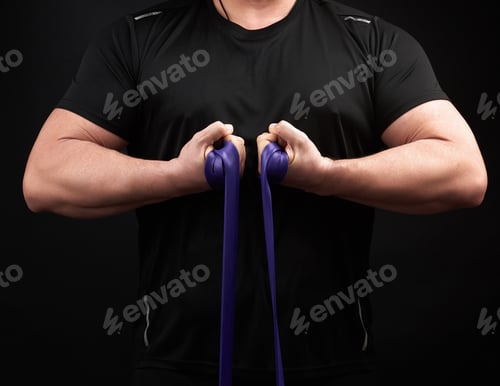 Preview: Athlete With A Muscular Body In Black Clothes Is Doing Physical Exercises With Blue Rubber, Low Key