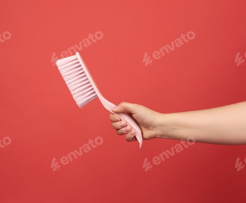 Preview: Female Hand Holds Pink Plastic Cleaning Brush, Red Background
