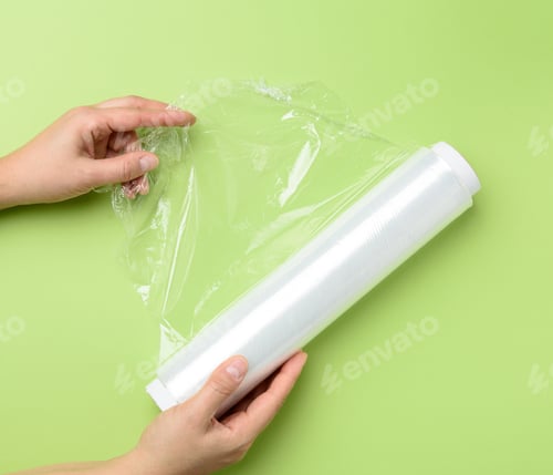 Preview: Two Female Hands Hold A Roll Of Transparent Cling Film For Packaging Products, Green Background