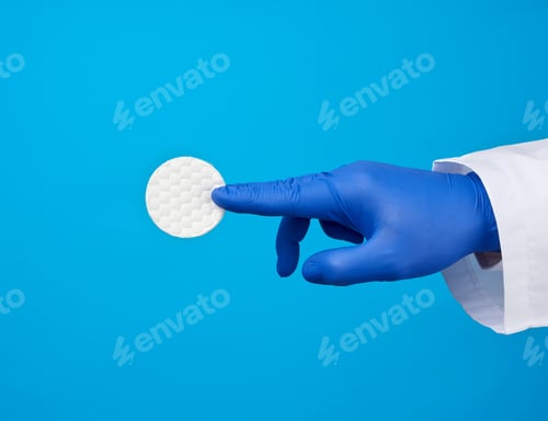 Preview: Hand Hold White Cotton Round Disc For Cosmetic Procedures On A Blue Background, Close Up