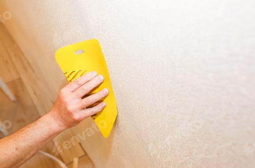 Preview: Man Is Using Scraper To Install Wallpaper. Levelling Of The Wall. Maintenance Repair Works