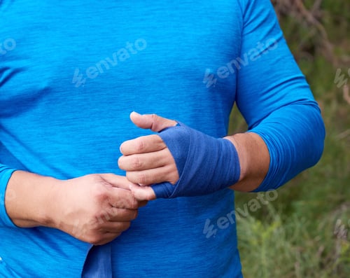 Preview: Athlete Stand And Wrap His Hands In Blue Textile Elastic Bandage Before Training,Sunny Summer Day