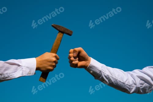 Preview: Hand Holding A Big Hammer Against A Blue Sky Background.