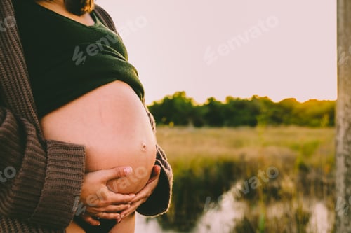 Preview: Belly Of Pregnant Mother With Hands Stroking At Sunset.