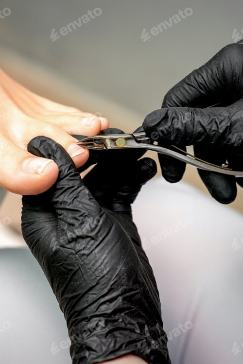 Preview: Closeup Of A Pedicure Master Is Cutting And Removing Cuticle With Nail Tongs On Female Toes In A