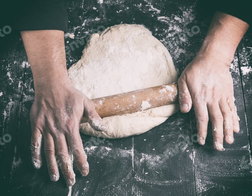 Preview: Chef In A Black Tunic Rolls A Dough For A Round Pizza, Top View