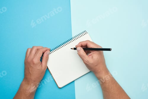 Preview: Two Male Hands Holding Open Notepad With Empty White Sheets On A Blue Background, Top View