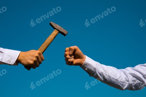 Preview: Hand Holding A Big Hammer Against A Blue Sky Background.