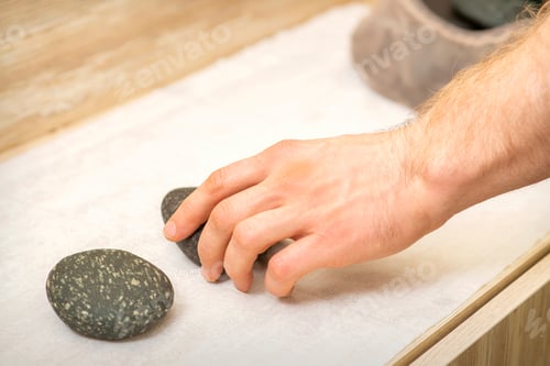 Preview: Hand Of Massage Therapist Taking Massage Stones From The Table Before Massage Procedures