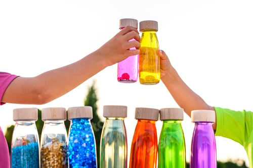 Preview: Happy Kids Toasting With Toy Bottles Of Vibrant Colors With Blue Sky Background.