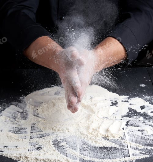 Preview: Chef In Black Uniform Pours White Wheat Flour Out Of His Hands On A Wooden Table, Product Flies To
