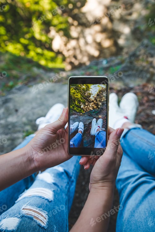 Preview: Couple Sitting On The Ground Taking Picture Of Legs On Phone. Lifestyle Concept