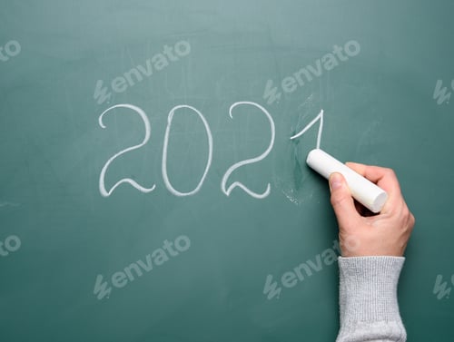 Visualização: Mão feminina segura um pedaço de giz branco e escreve em um quadro escolar verde 2021, Ano Novo