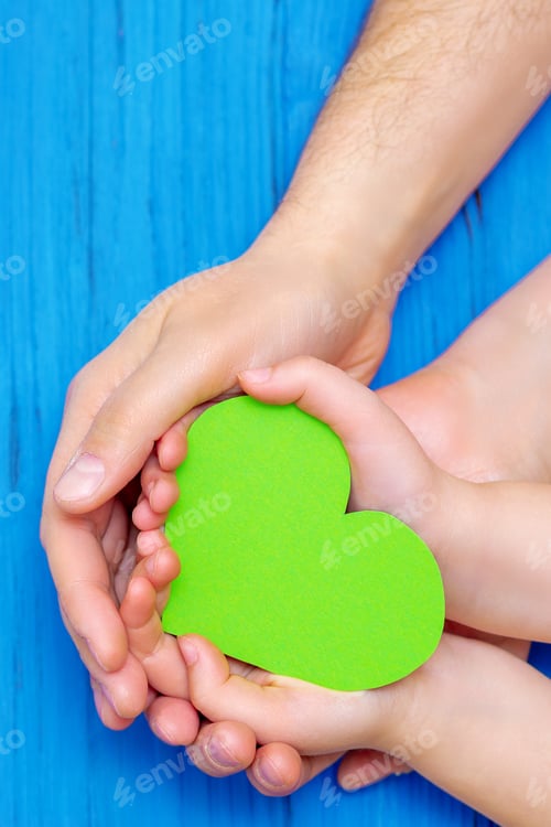 Vista previa: Close Up Of Male And Child Hands Holding Paper Green Heart On Wooden Blue Background. Concept Of
