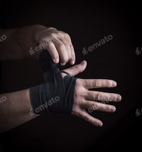 Preview: Man Wraps His Hands In Black Textile Bandage For Sports, Black Background
