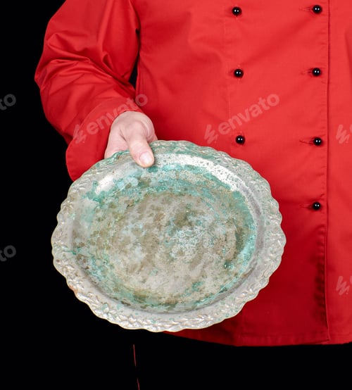 Preview: Chef In Red Uniform Holds In His Hand An Empty Iron Round Dish, Black Background