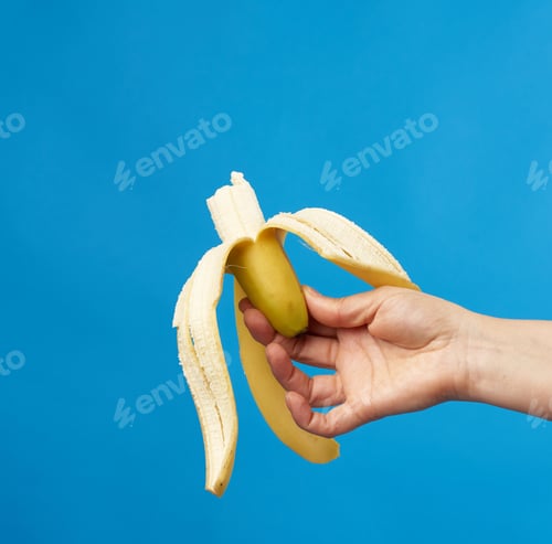Preview: Female Hand Holds A Ripe Peeled Banana On A Blue Background, Close Up