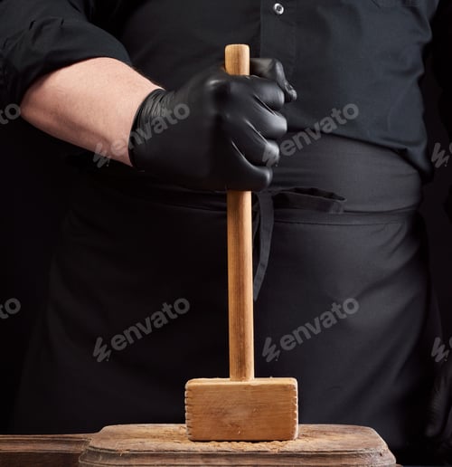 Preview: Cook In Black Uniform Holds A Wooden Hammer For Beating Meat On A Vintage Cutting Board, Black
