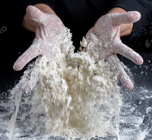 Preview: Chef In Black Uniform Pours White Wheat Flour Out Of His Hands On A Wooden Table, The Product Flies