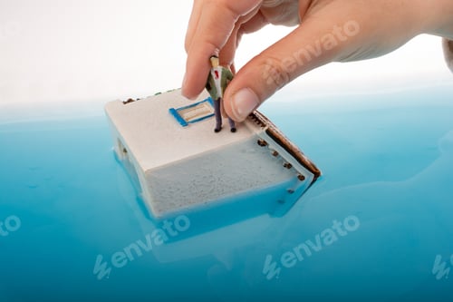Preview: Hand Holding A Man Figurines In Water By On The Roof Of A Model House