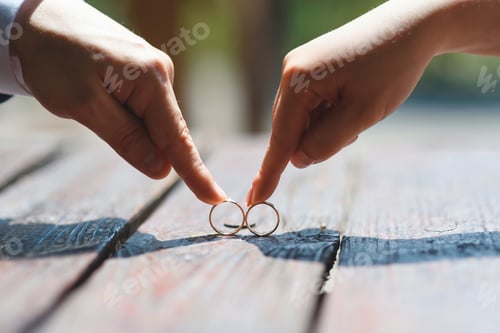 Preview: Bride And Groom Holding Wedding Rings By Fingers On Wooden Table In Sunlight