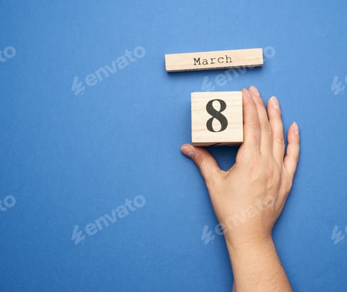 Preview: Female Hand Holds Wooden Calendar With Date Of Eighth March On Blue Background