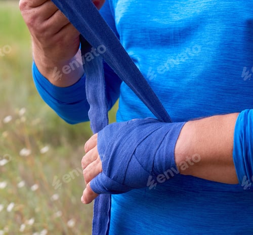 Preview: Athlete Stand And Wrap His Hands In Blue Textile Elastic Bandage Before Training, Outdoor