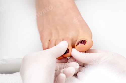 Preview: Manicure Master Holds Female Toenail With Maroon Nail Polish Wearing White Gloves
