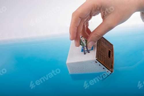 Preview: Hand Holding A Man Figurines In Water By On The Roof Of A Model House