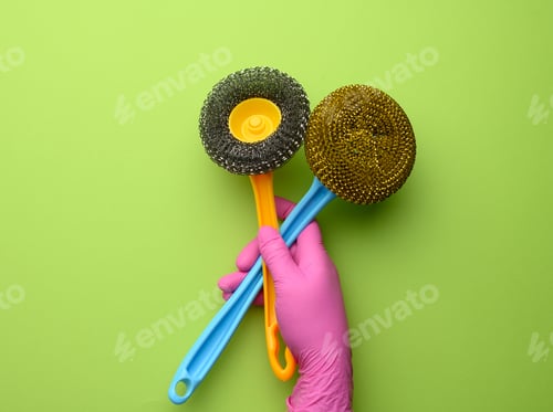 Preview: Female Hand In Purple Rubber Gloves Holds A Plastic Cleaning Brush On Green Background, Close Up