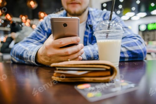 Preview: Man Searfing Phone On Background Wallet With Cup Of Milk Shake On The Table In Front
