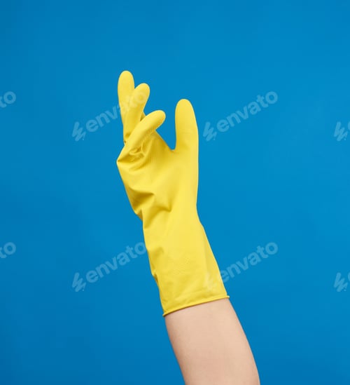 Preview: Yellow Rubber Glove For Cleaning Dressed On A Female Hand, Blue Background, Part Of The Body Raised