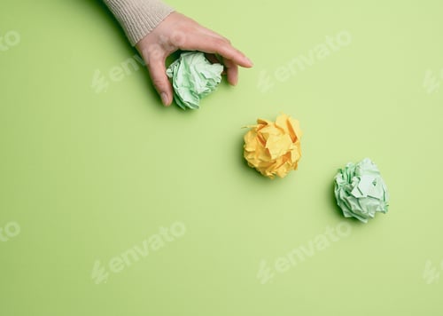 Preview: Three Crumpled Balls Of Colored Paper On A Green Background, Hand Throws Paper