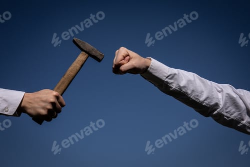 Preview: Hand Holding A Big Hammer Against A Blue Sky Background.