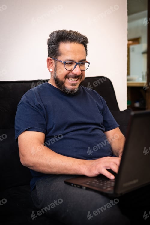Preview: A Happy Latino Man Living With Hiv Sitting On His Sofa Using A Laptop